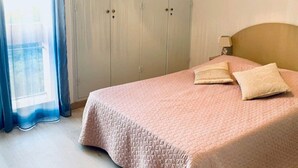 A bedroom with a bed, a wardrobe, and a window with curtains. - Bright F2 Apartment with Terrace, Parking, and WiFi in Amélie-les-Bains (Amélie-les-Bains-Palalda)