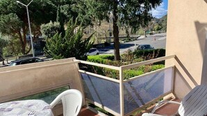 A balcony with a table and two chairs, a view of a street with cars, and trees in the background. - Bright F2 Apartment with Terrace, Parking, and WiFi in Amélie-les-Bains (Amélie-les-Bains-Palalda)