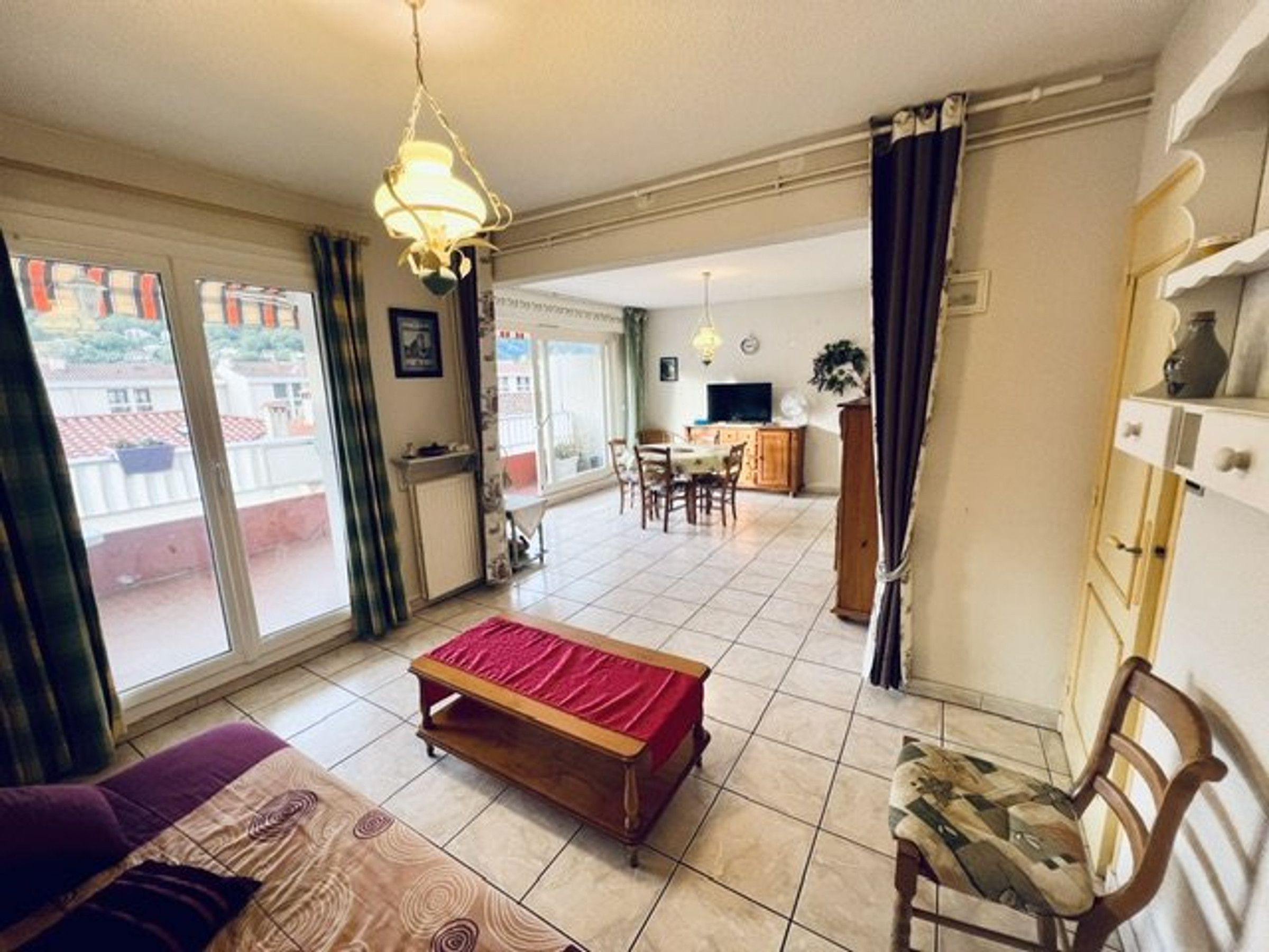 A spacious living area with a sofa, a bench, a dining table, and a kitchen in the background.