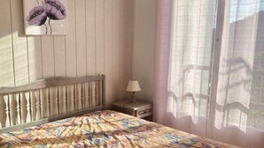 A bedroom with a bed, a nightstand, a lamp, a window with curtains, and a wall-mounted picture. - Cozy F2 Apartment with Parking, Balconies, and WIFI Near Thermal Baths (Amélie-les-Bains-Palalda)