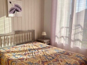 A bedroom with a bed, a nightstand, a lamp, a window with curtains, and a wall-mounted picture.