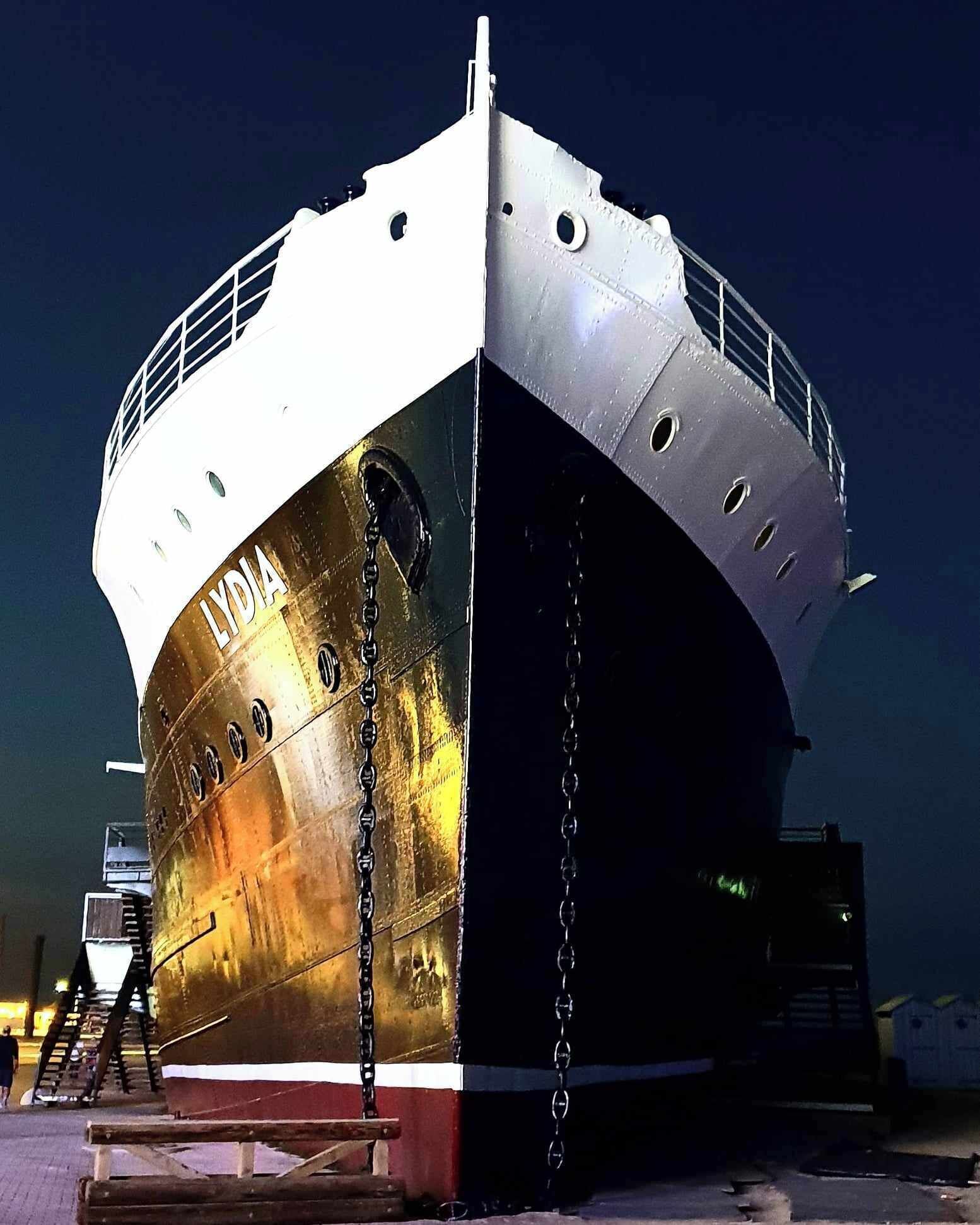 A large ship named 'LYDIA' docked at a port with a chain securing it to the dock.