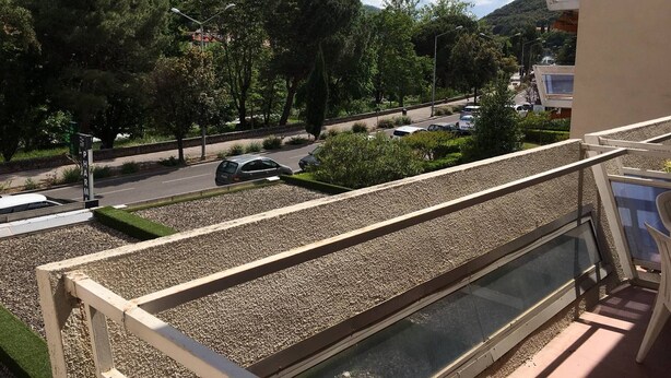 A balcony with a view of a road, parked cars, and a mountain in the background.