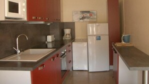 A compact kitchen with red cabinets, a white microwave, a coffee maker, and a refrigerator.