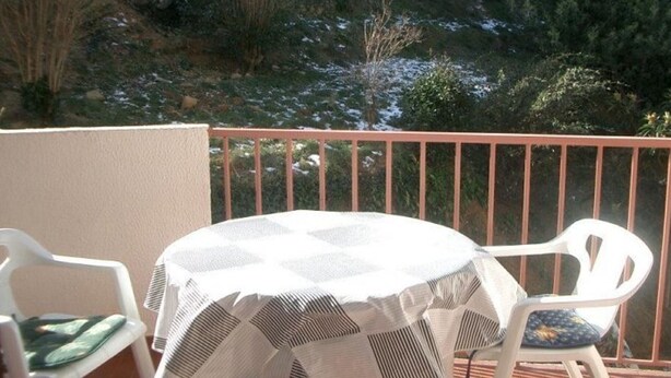 A balcony with a table and chairs, a railing, and a view of a snowy landscape with trees.