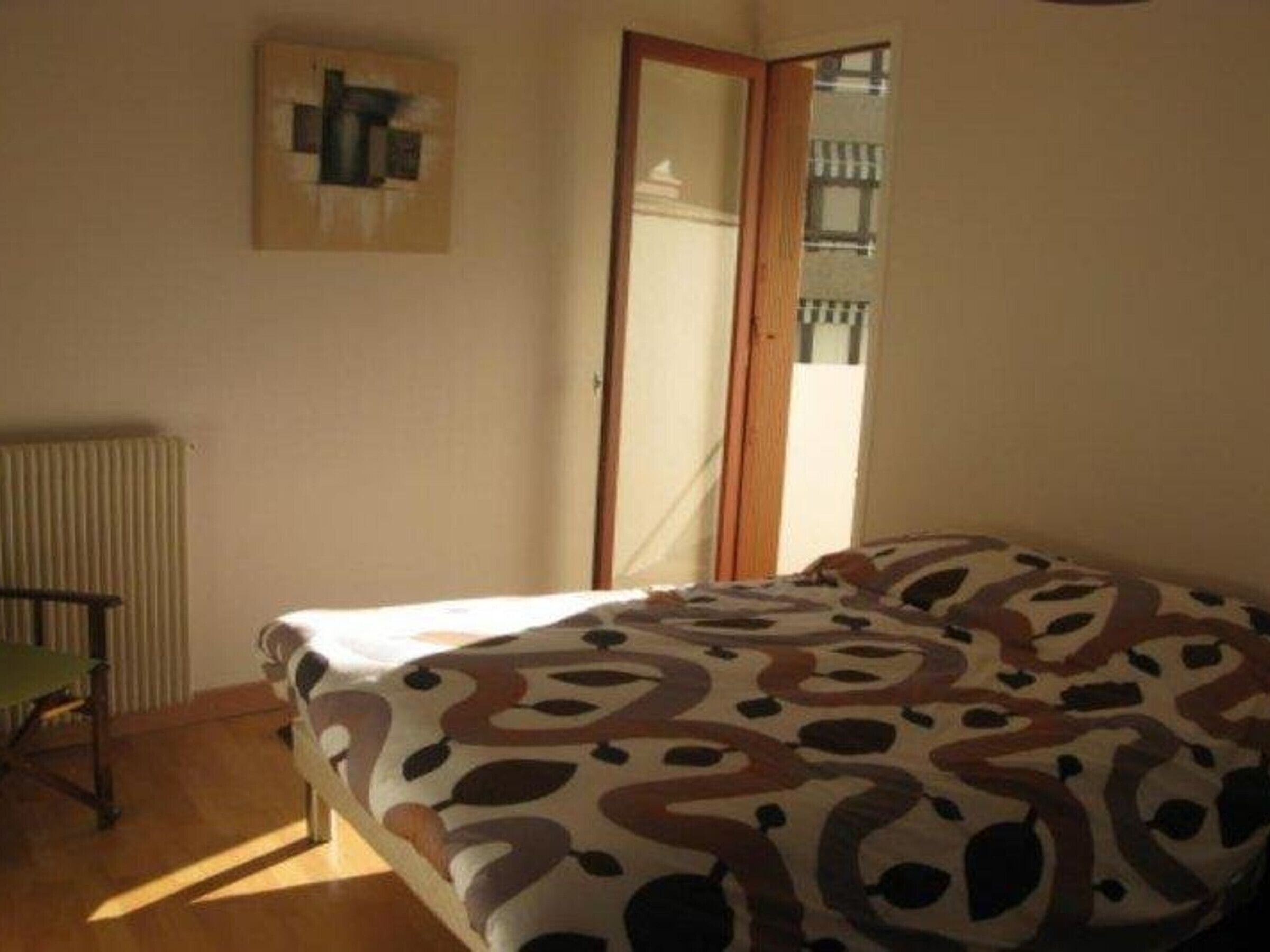 A bedroom with a bed, a radiator, a chair, and a door leading to a balcony.