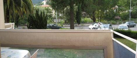 A balcony with a view of a street, parked cars, and trees.