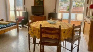 Une pièce dotée d’une table ronde, de chaises, d’un téléviseur et offrant une vue sur un paysage montagneux grâce à de grandes fenêtres.