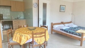 Une petite pièce compacte comprenant un coin cuisine, une table à manger avec des chaises et un lit simple.