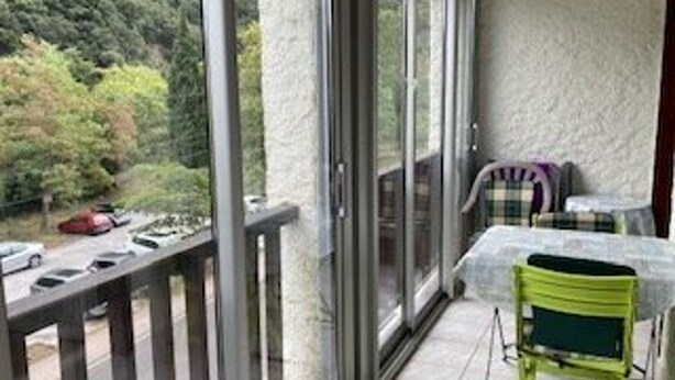 Un balcon avec une table et des chaises, une voiture rouge garée devant, et une vue sur la verdure.