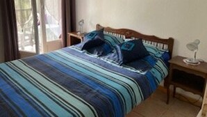 A bedroom with a bed, a nightstand, a lamp, and a window with curtains. - Comfortable F2 Apartment with Parking and Pets Allowed (Amélie-les-Bains-Palalda)
