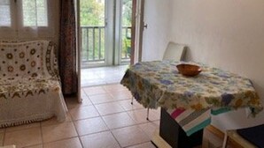 Une pièce avec un canapé, une table recouverte d’une nappe à motifs floraux et une vue sur la verdure, visible à travers une porte vitrée.