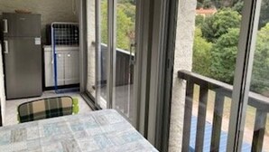 Un balcon avec une table et des chaises, une petite kitchenette et une vue sur la verdure.