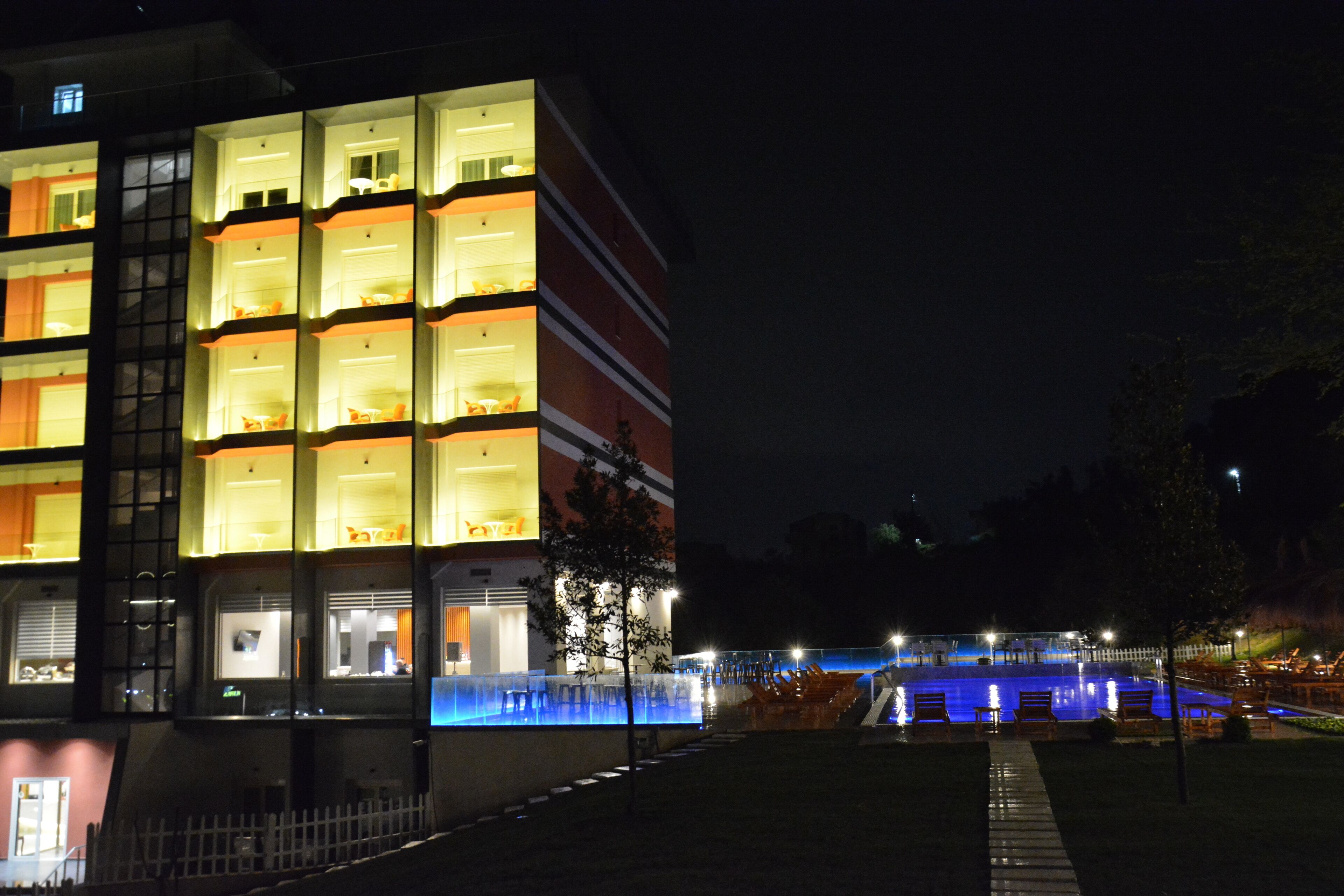 A multi-story hotel with illuminated balconies, a swimming pool, and outdoor seating.