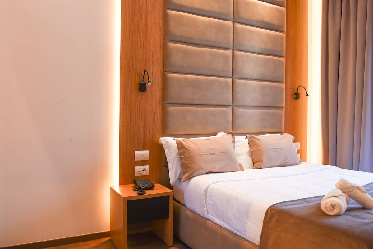 Een hotelkamer met een groot bed, een houten nachtkastje met telefoon en een hoofdeinde met ingebouwde verlichting.
