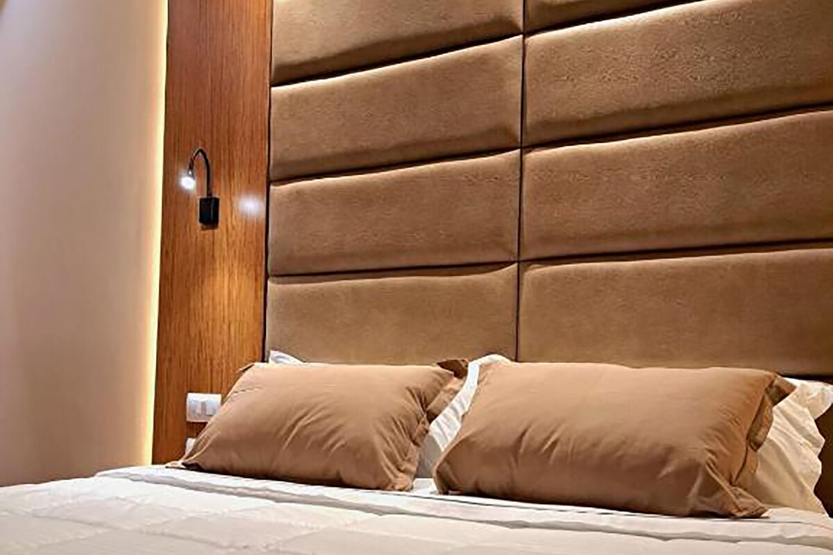 Quarto com uma cama grande, cabeceira de madeira e luminária fixada na parede.