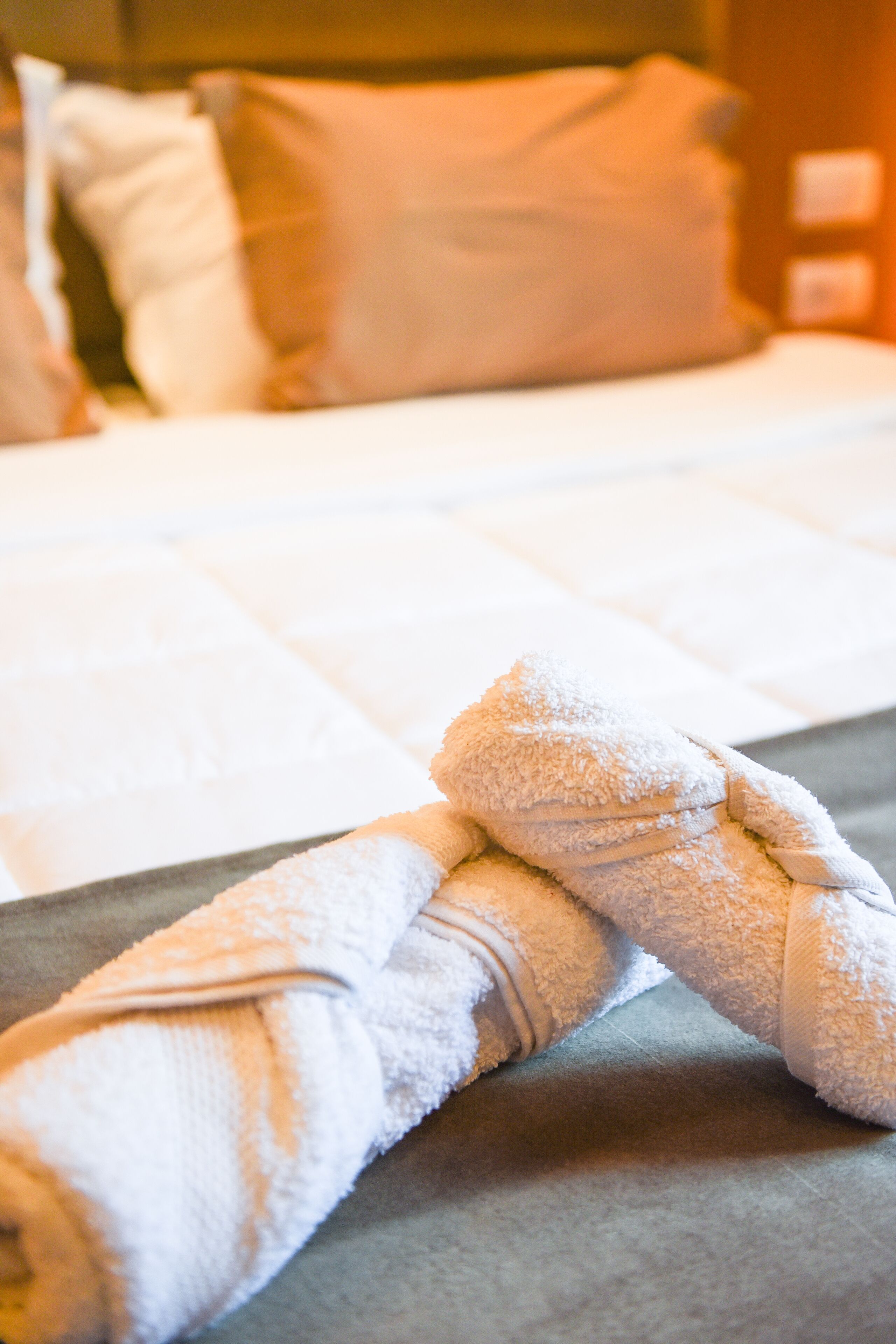 A neatly made bed with white linens and a folded towel on the bed.