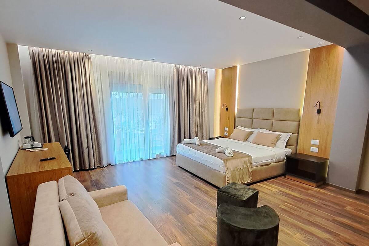 Een moderne hotelkamer met een sofa, een bed, een houten salontafel en een televisie op een houten standaard.