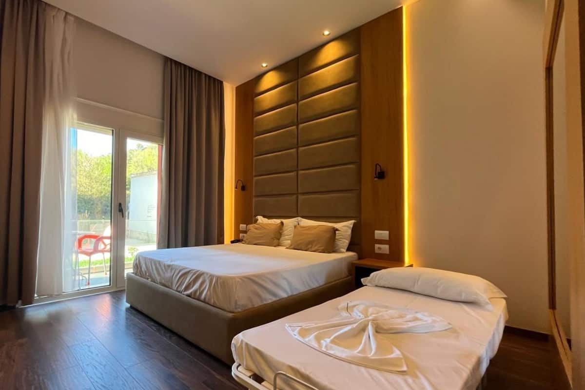 Een hotelkamer met twee bedden, een schuifdeur naar buiten en een houten hoofdeinde.