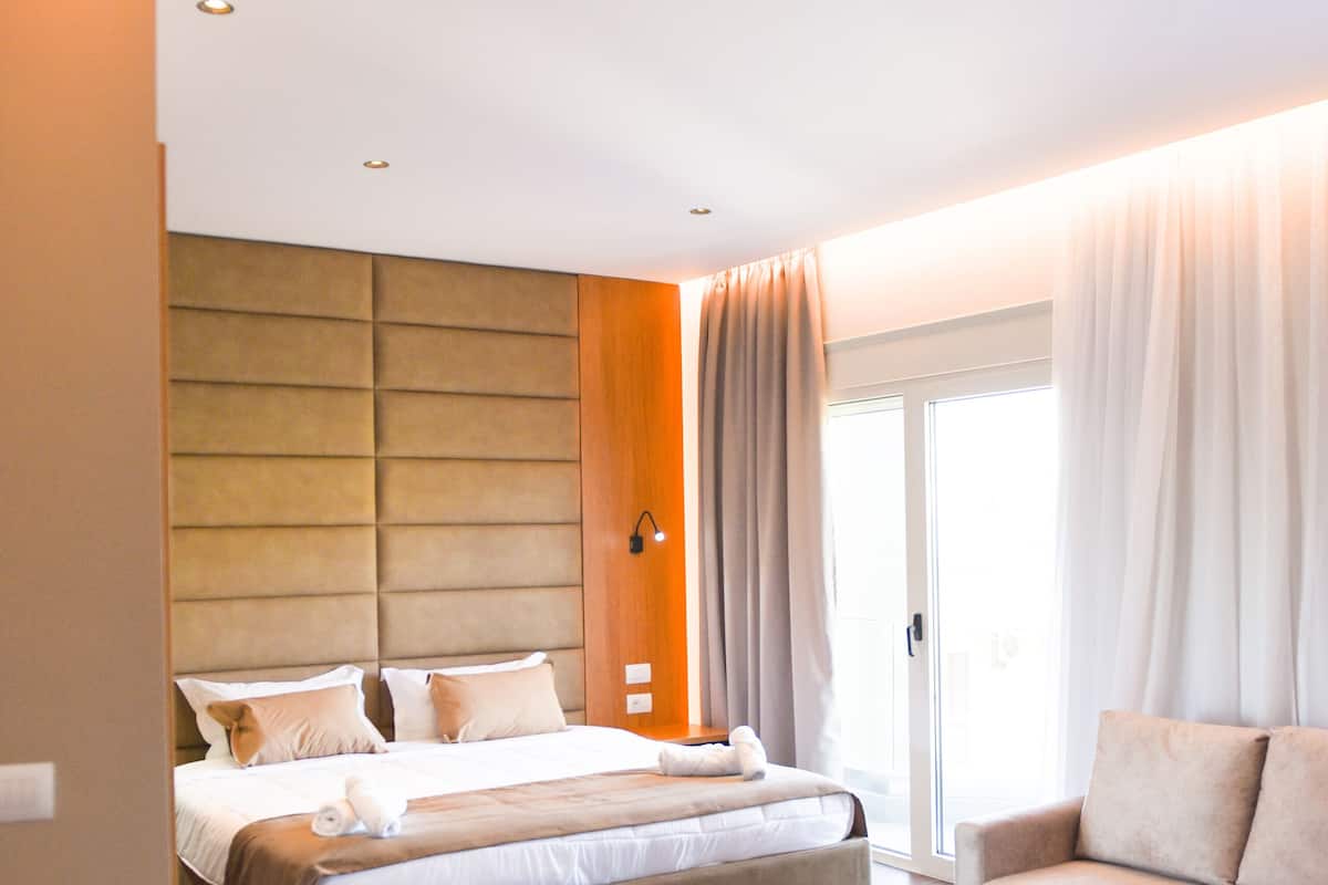 Een moderne hotelkamer met een groot bed, een sofa en een klein pouf.