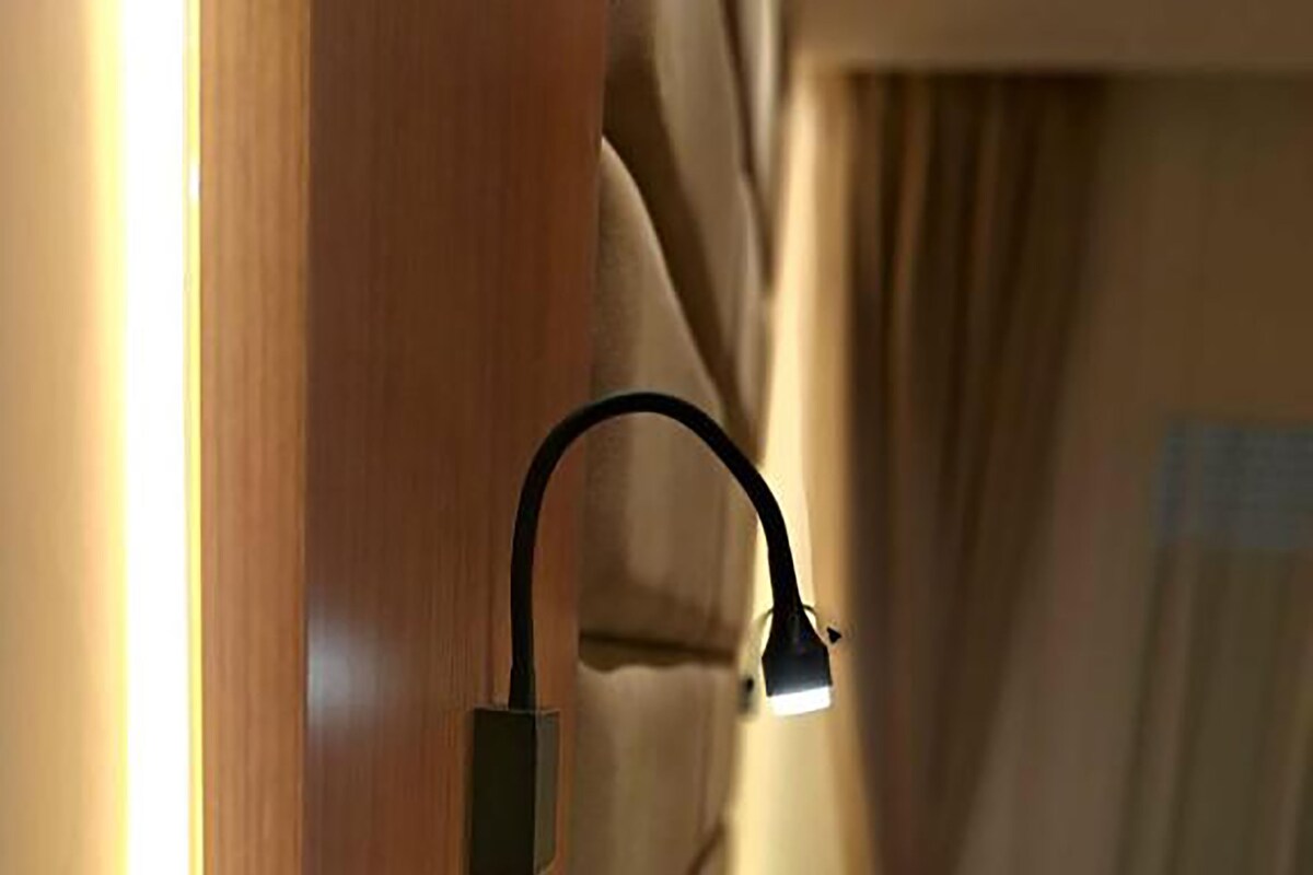 Een bed met hoofdeinde, een bedlamp en een gordijn dat gedeeltelijk het raam verbergt.