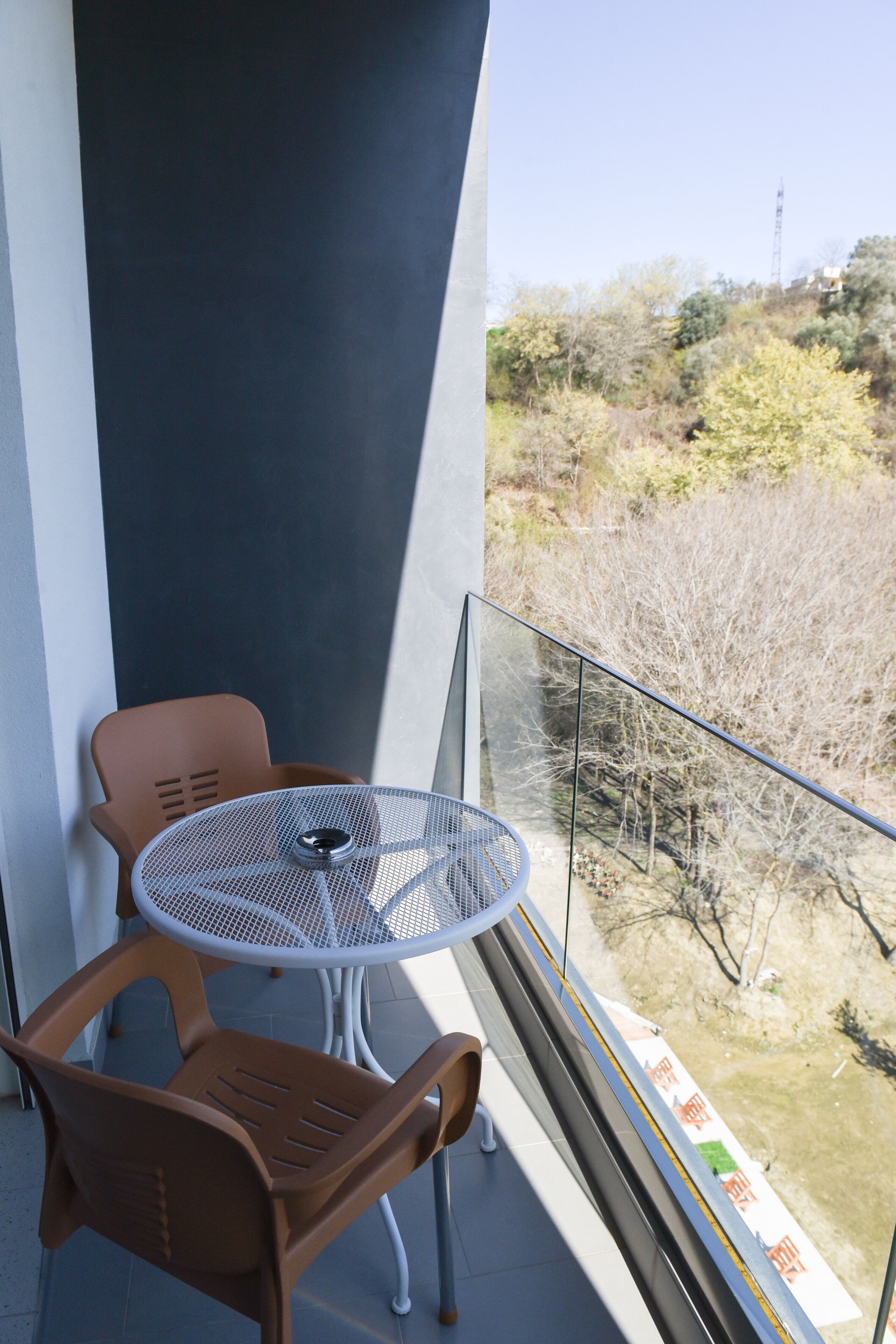 En balkon med et bord og stole, udsigt til træer og et fjernt tårn.