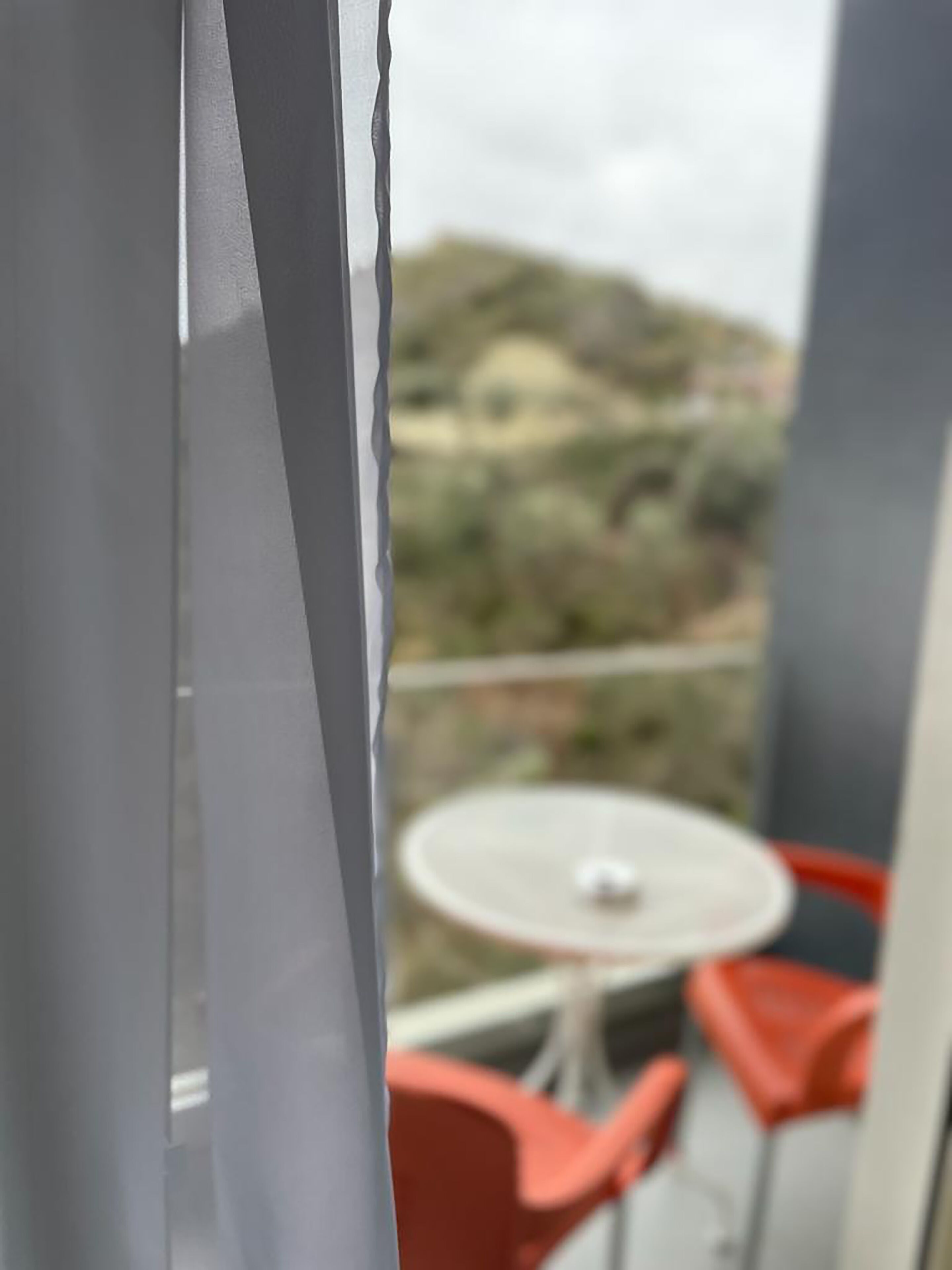 A balcony with a table and red chairs, overlooking a hilly landscape.