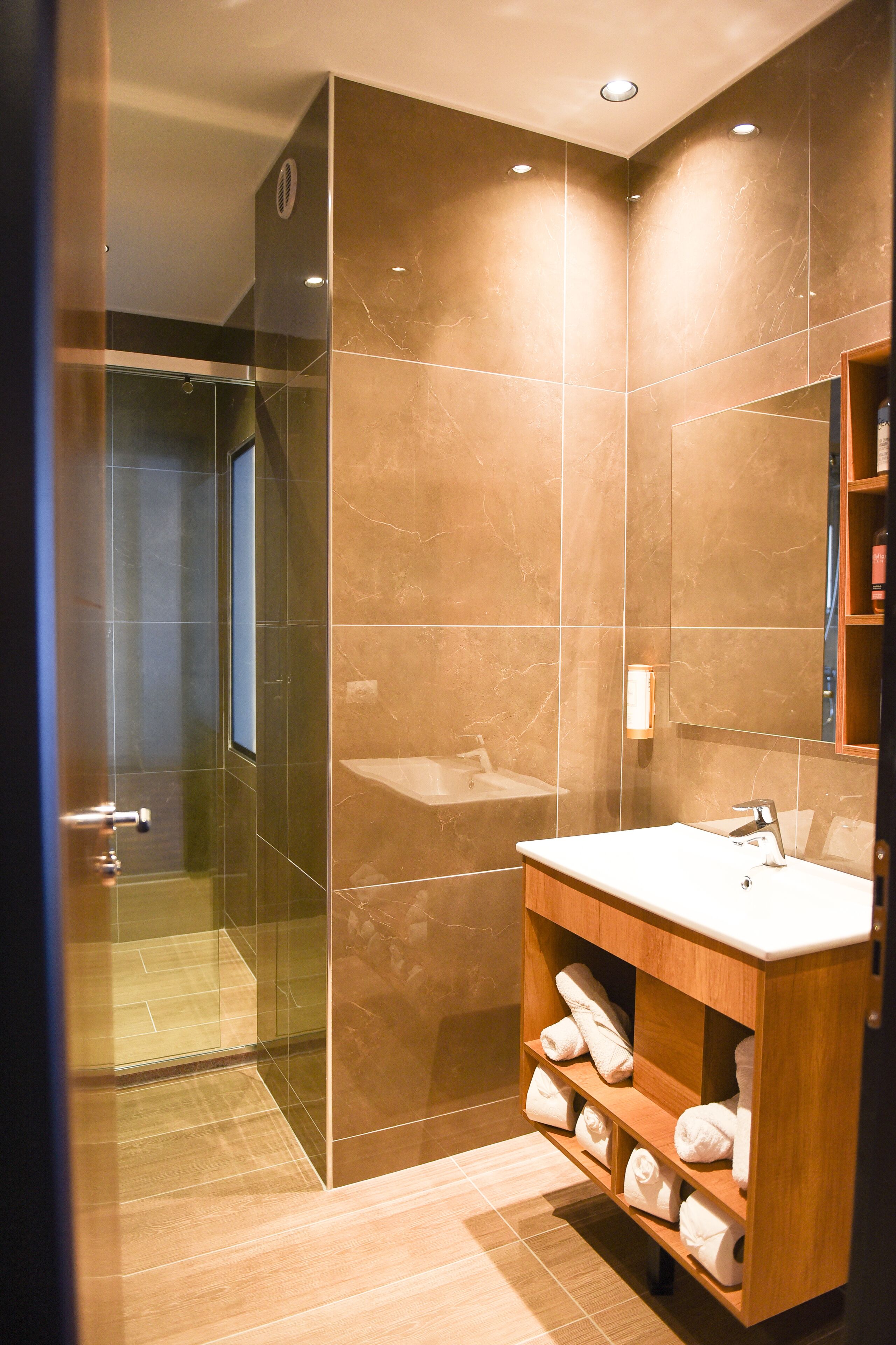 Un bagno moderno con cabina doccia in vetro, mobile lavabo in legno e parete rivestita in marmo.