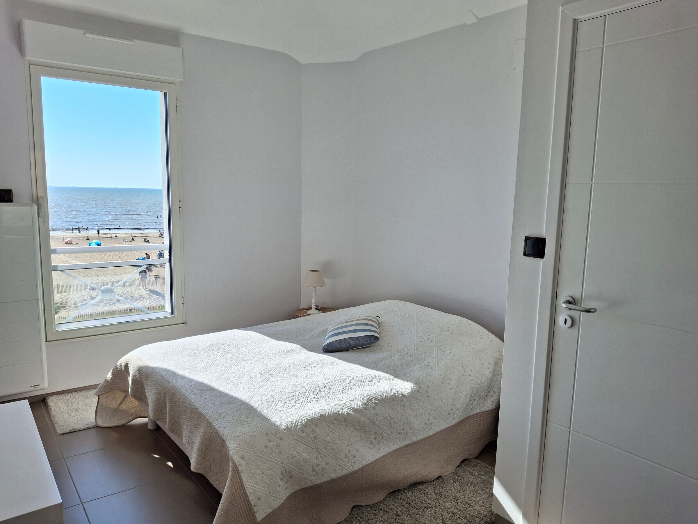 Une chambre avec un lit, une fenêtre donnant sur la plage et une porte.