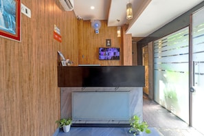 A reception desk with a flat-screen TV, wooden paneling, a fan, and a glass door. - Hotel Signature Inn (Mumbai)