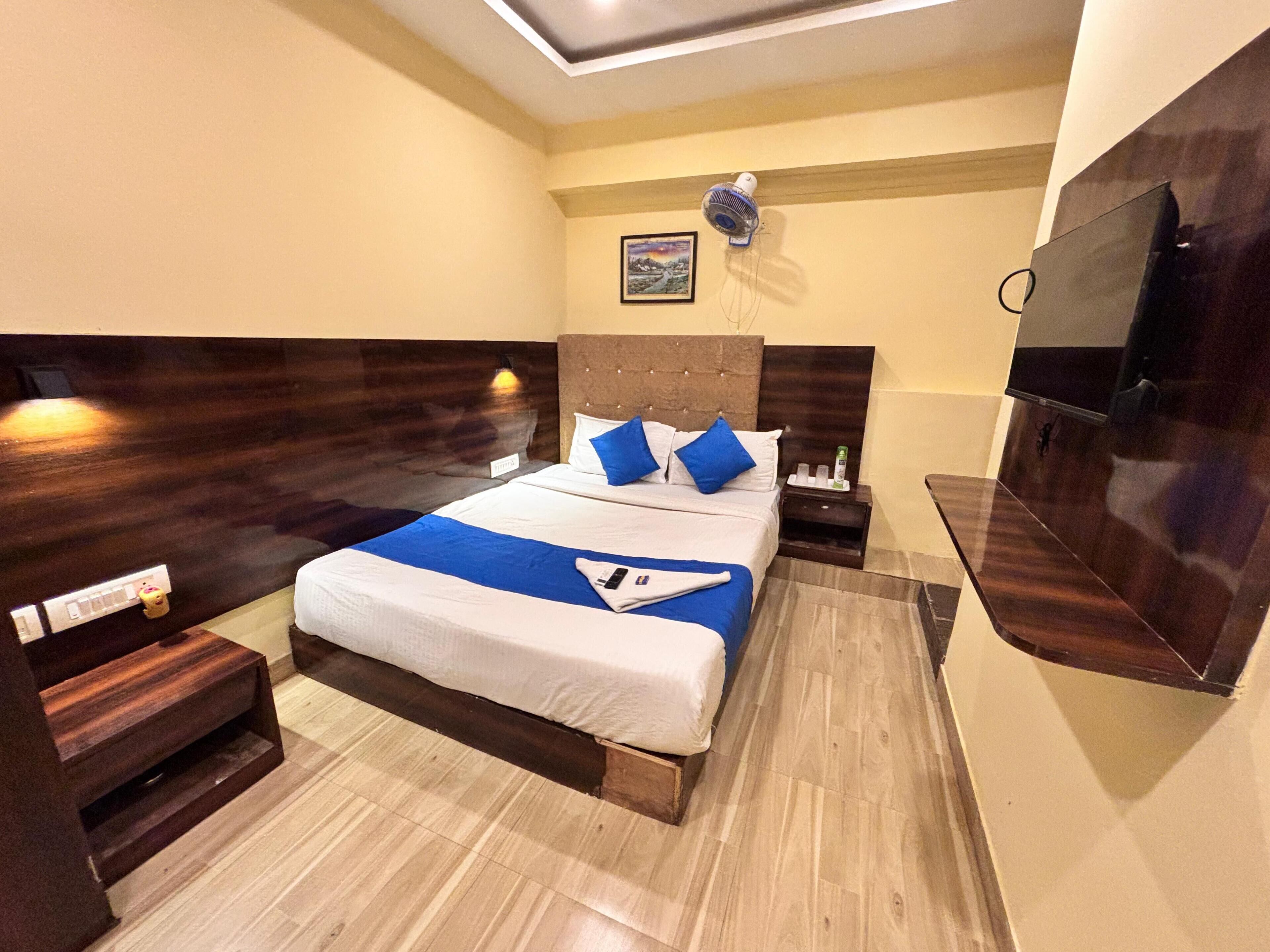 A hotel room with a large bed, wooden headboard, bedside tables, a TV, and a ceiling light.