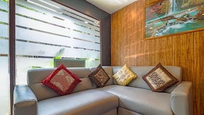 A modern living room with a sectional sofa, decorative pillows, a wooden accent wall, and a framed landscape painting. - Hotel Signature Inn (Mumbai)