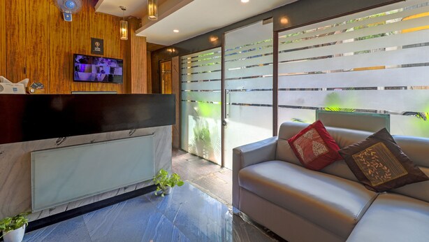 A reception area with a wooden wall, a reception desk, a flat-screen TV, and a sofa with decorative pillows. - Hotel Signature Inn (Mumbai)