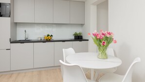 Et moderne køkken med hvide skabe, en sort bordplade og et hvidt spisebord med stole. Der står en vase med blomster på bordet.