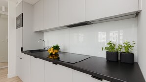 Et moderne køkken med hvide skabe, en sort bordplade, en stålvask og to krukker med planter.