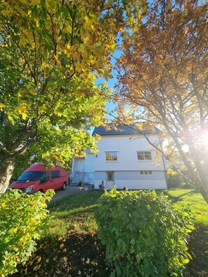A white two-story house with a blue roof, a red van parked in front, and a well-maintained lawn. - Private house in picturesque surroundings (Nordland)