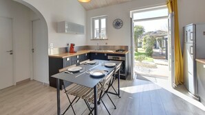A modern kitchen with a wooden ceiling, a large island, and a view of a garden through the open door. - Beachside Villa with Pool - 2BR, 4 Guests, Near Market & Beach (Châtelaillon-Plage)