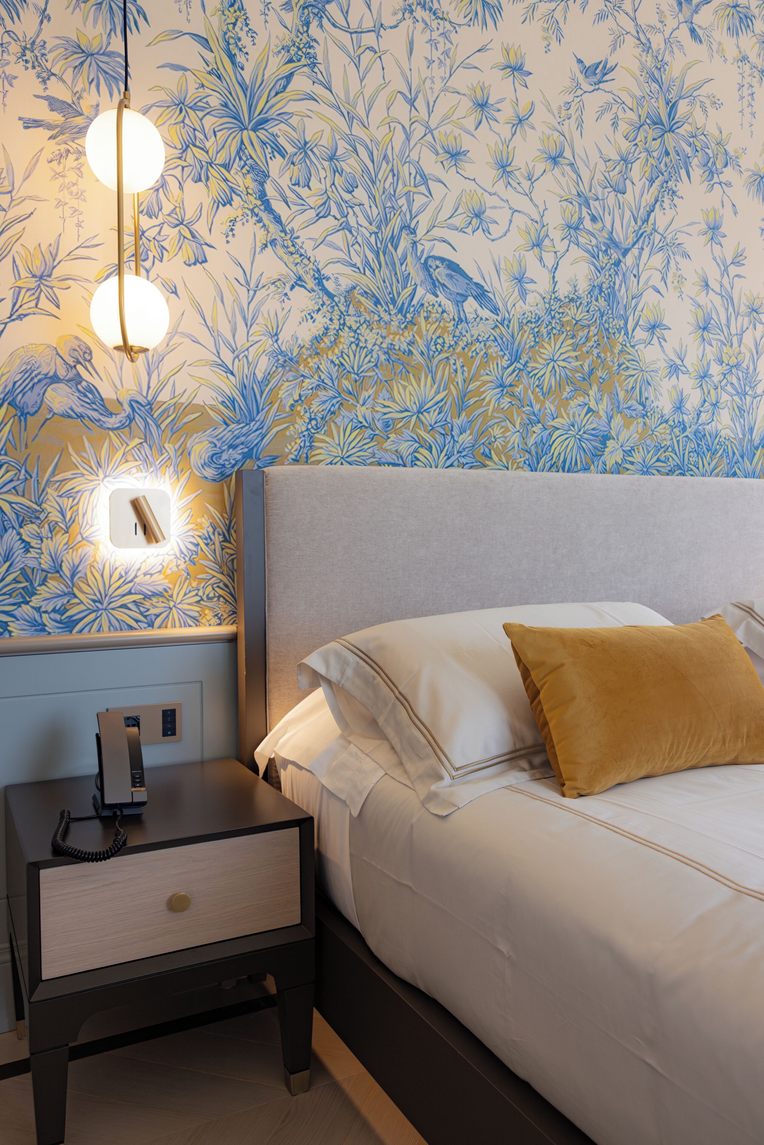 Un dormitorio con cama, mesita de noche y lámpara fijada a la pared.