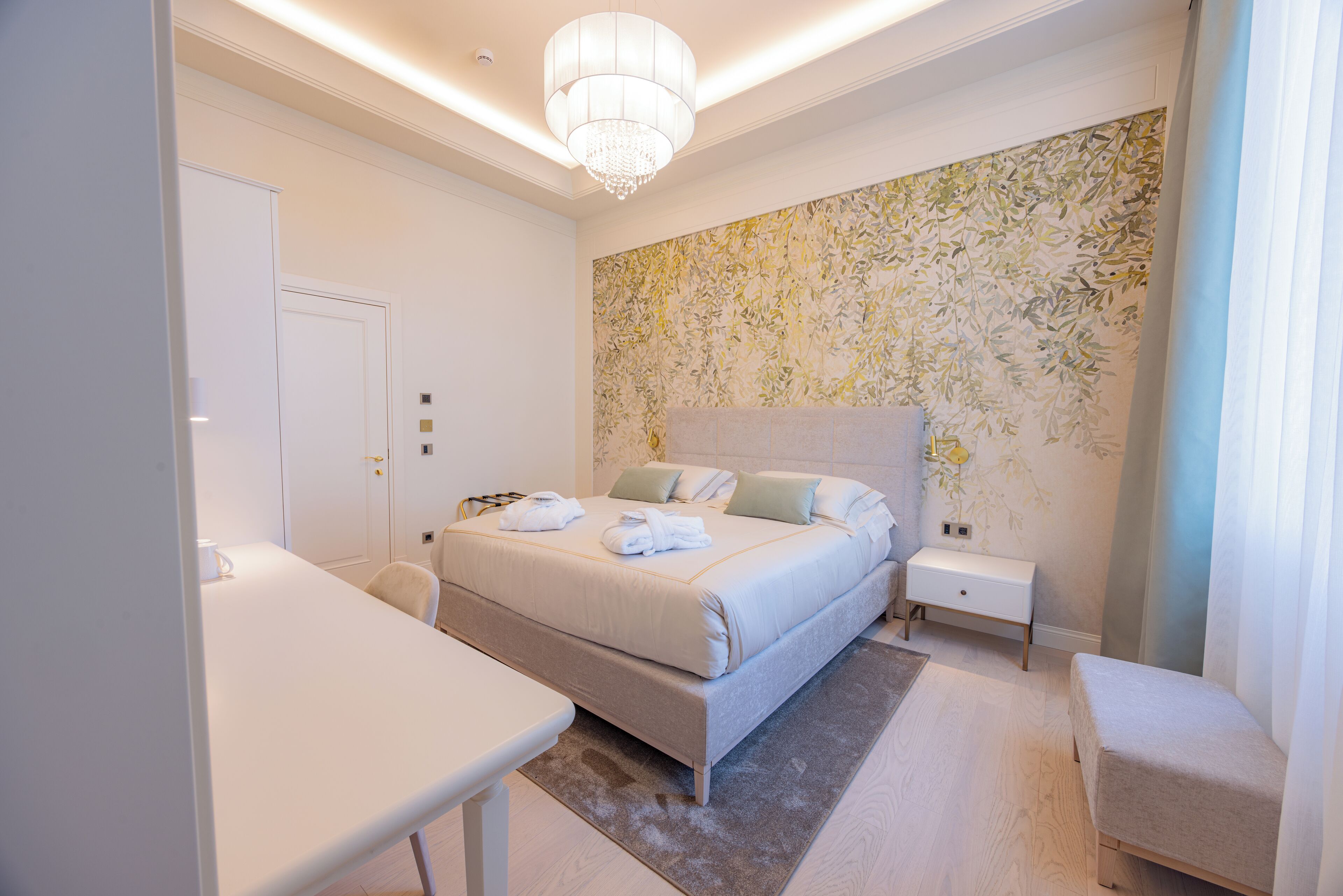 A modern bedroom with a large bed, bedside tables, a desk, and a chandelier.