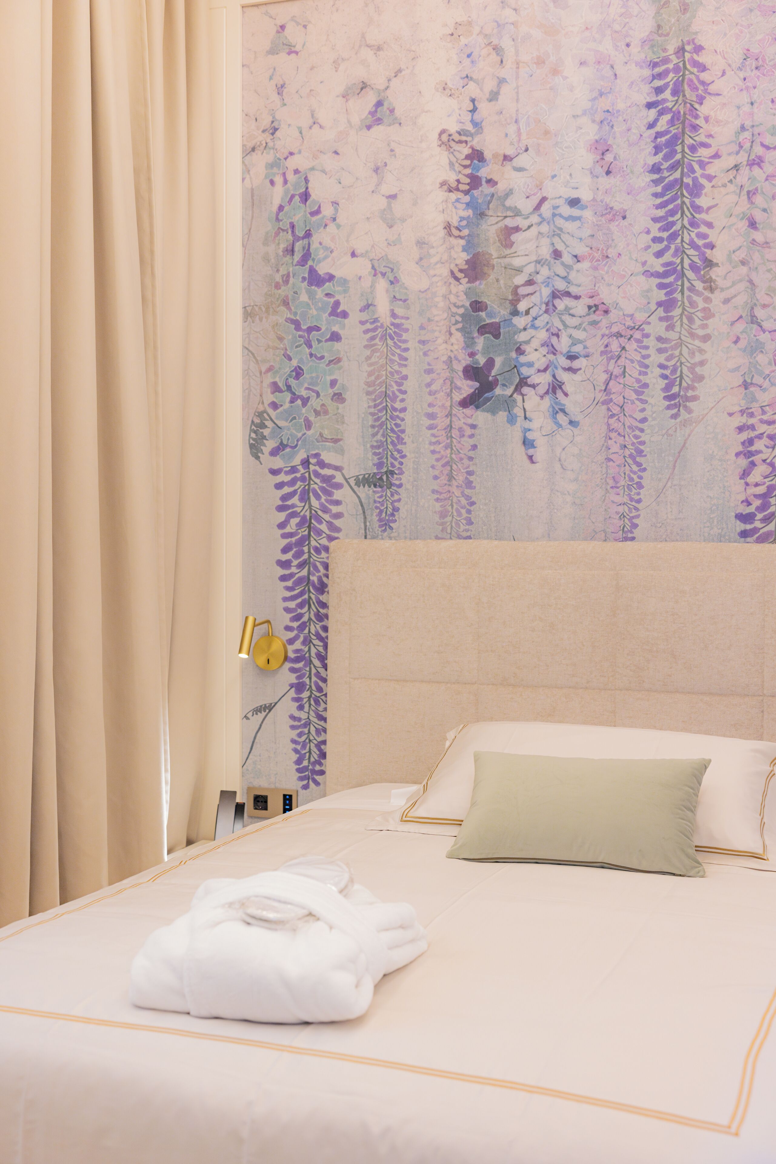 Una cama bien hecha con una almohada verde, una toalla blanca doblada y una pared con papel tapiz floral.
