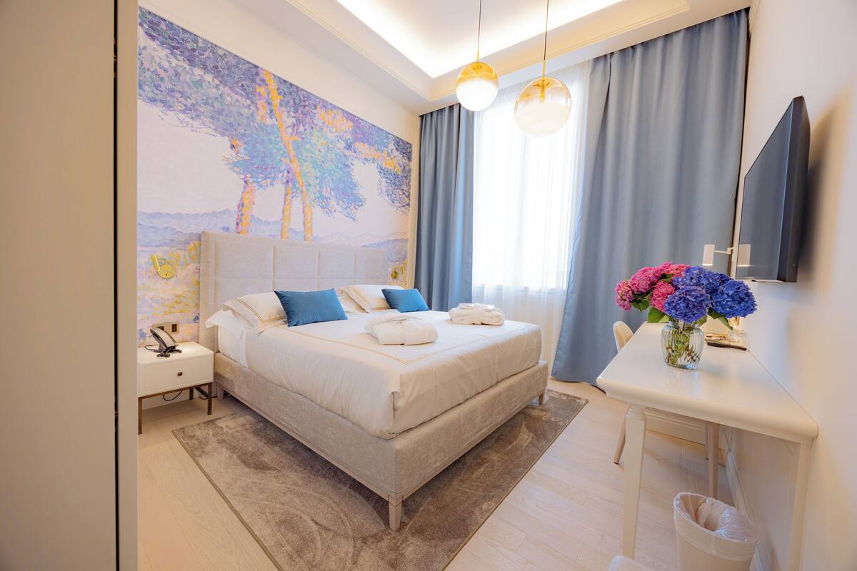 Une chambre d’hôtel moderne avec un grand lit, une table de chevet et un bureau agrémenté d’un vase de fleurs.