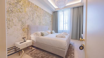 Ein modernes Schlafzimmer mit einem großen Bett, Nachttischen, einer Stehlampe, einer Chandelier und einem Fenster mit Vorhängen.