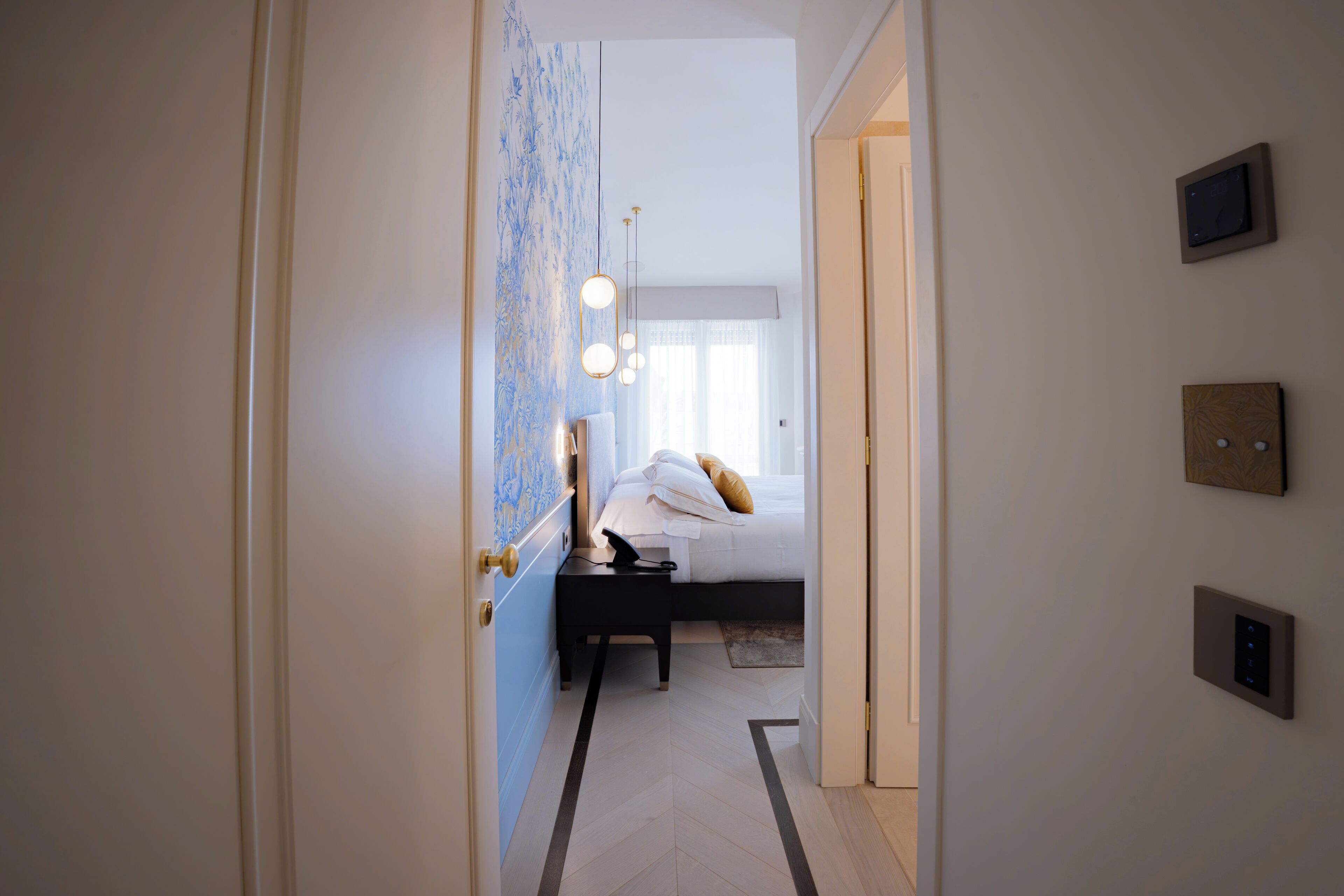 Una habitación de hotel con cama, mesita de noche y panel de control en la pared.