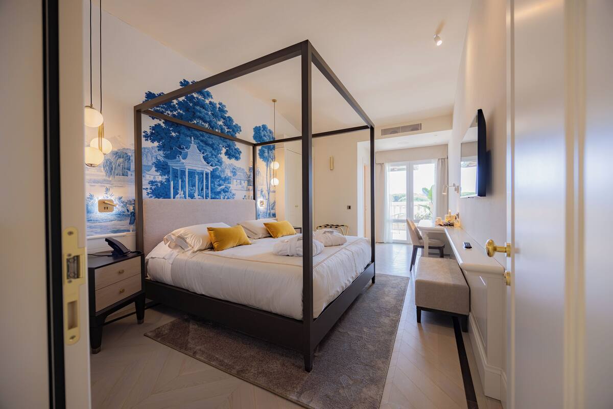 Une chambre à coucher moderne avec un lit à baldaquin, des tables de chevet, un bureau et une grande fenêtre.