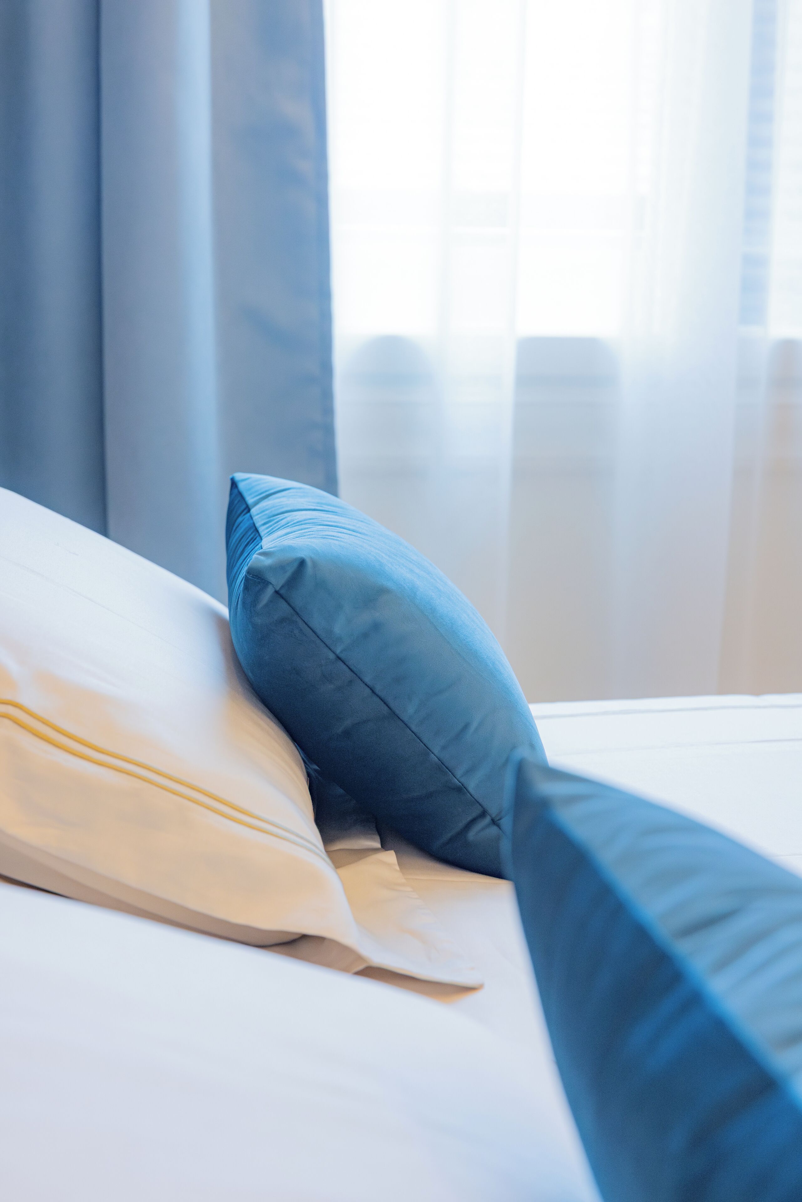 A bed with white and blue pillows, a white headboard, and a window with curtains.