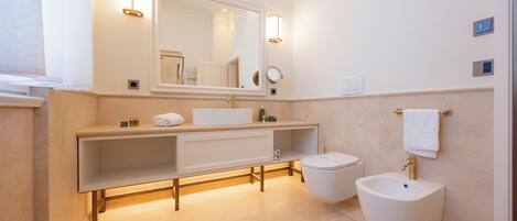 A modern bathroom with a large mirror, a vanity with a sink, a bidet, and a towel rack.
