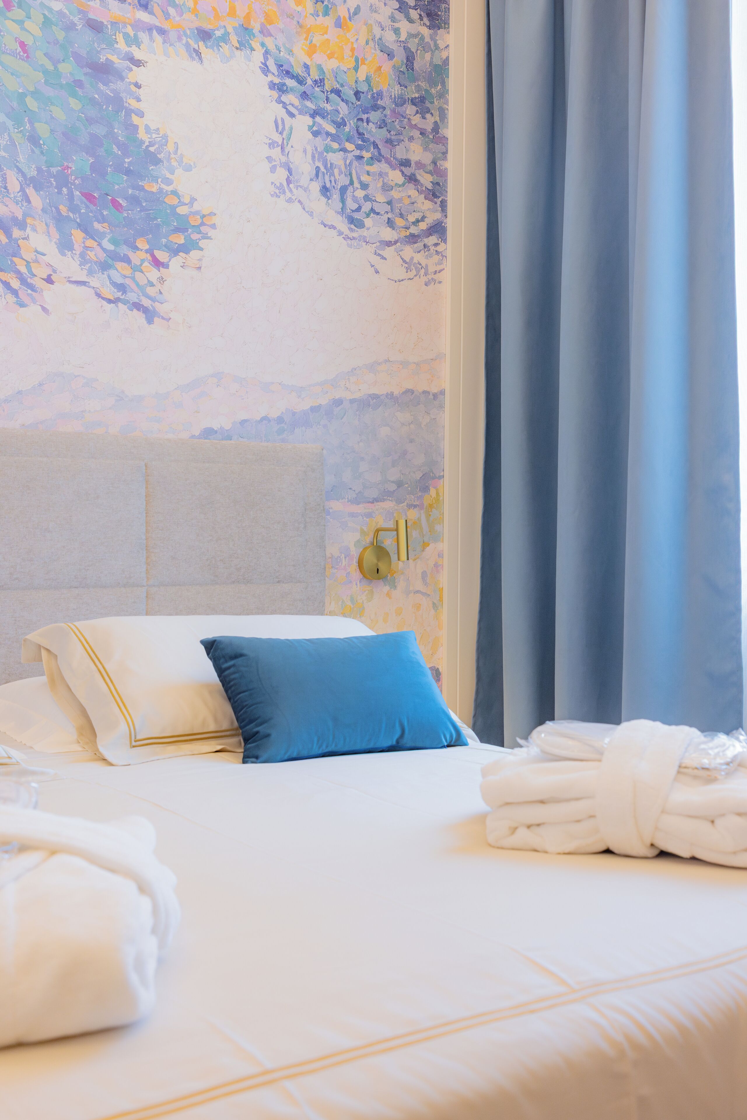 A hotel room with a neatly made bed, a headboard, and a wall with a floral pattern.