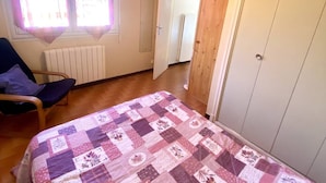 Makuuhuoneessa on sänky, tuoli, patteri, vaatekaappi ja ovi, joka johtaa toiseen huoneeseen.