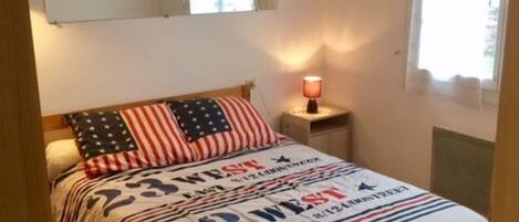 Een slaapkamer met een bed, nachtkastje, lamp en raam.