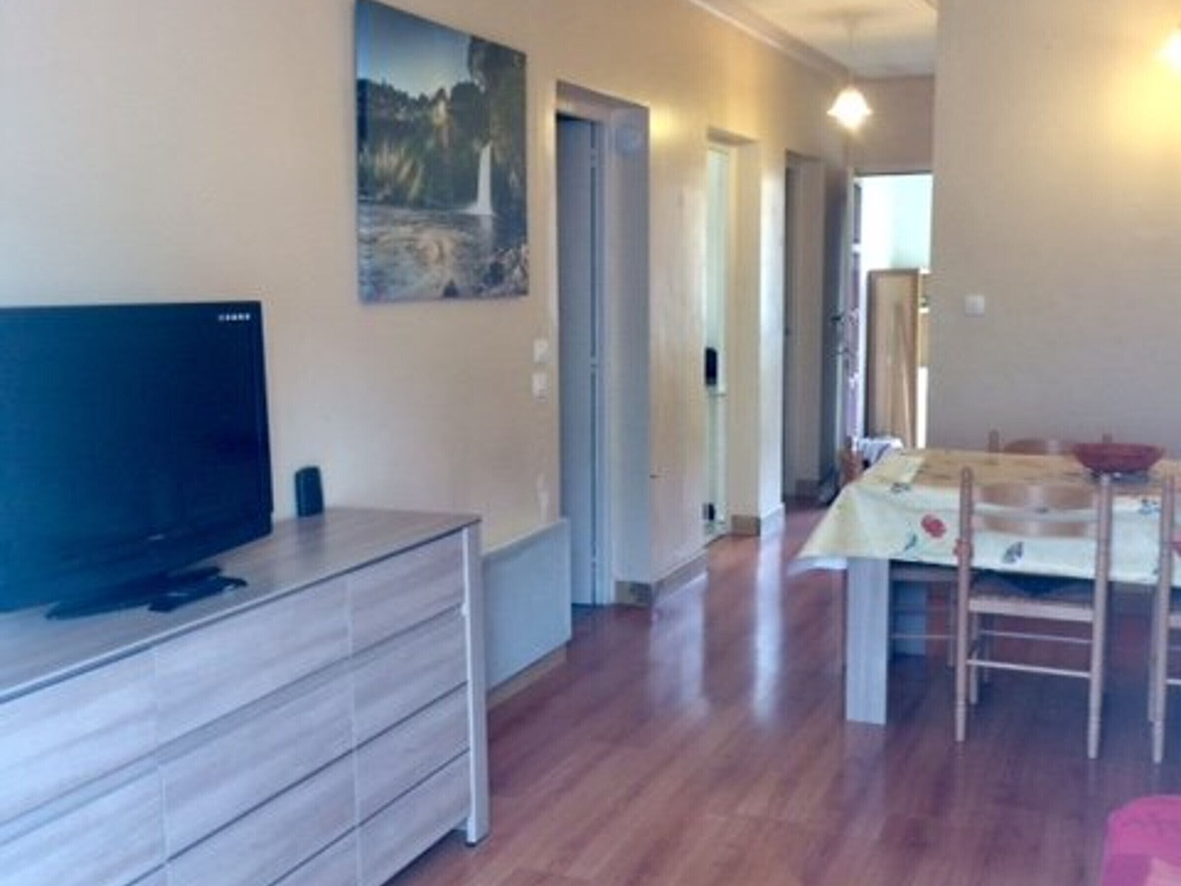 Una habitación con una televisión de pantalla plana sobre un mueble de madera, una mesa de comedor con sillas y un cuadro en la pared.